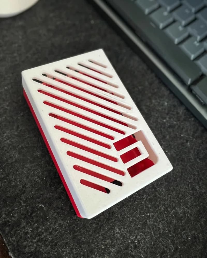 A red and white 3D-printed electronics case with slotted vents on a desk