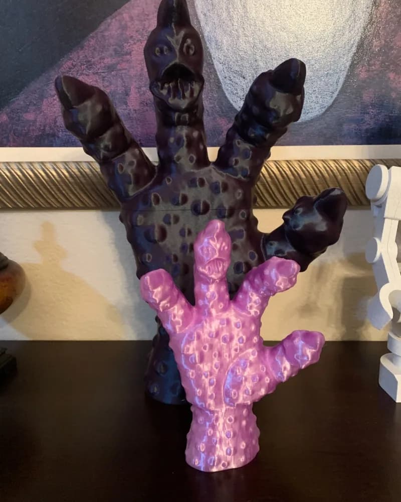 Two 3D-printed clawed creature figures, one purple and one black, on a shelf