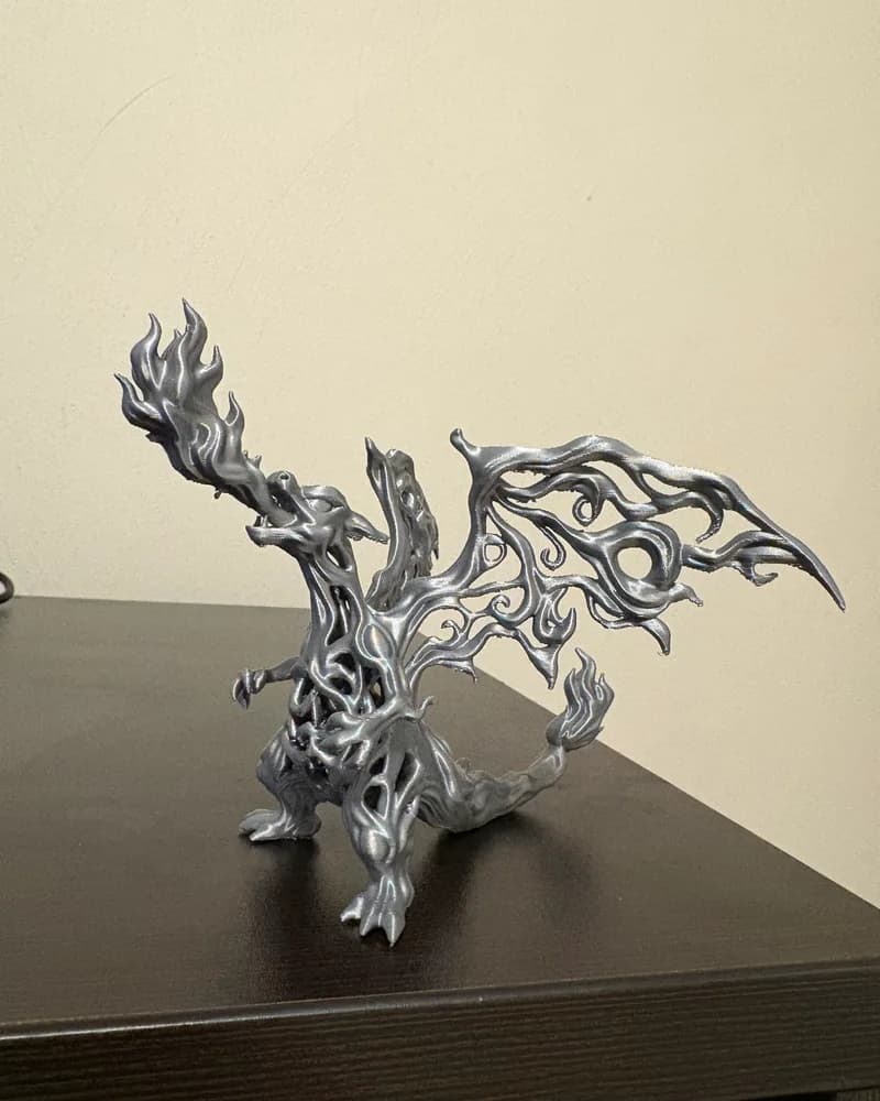 A silver 3D-printed dragon figurine breathing flames, on a table