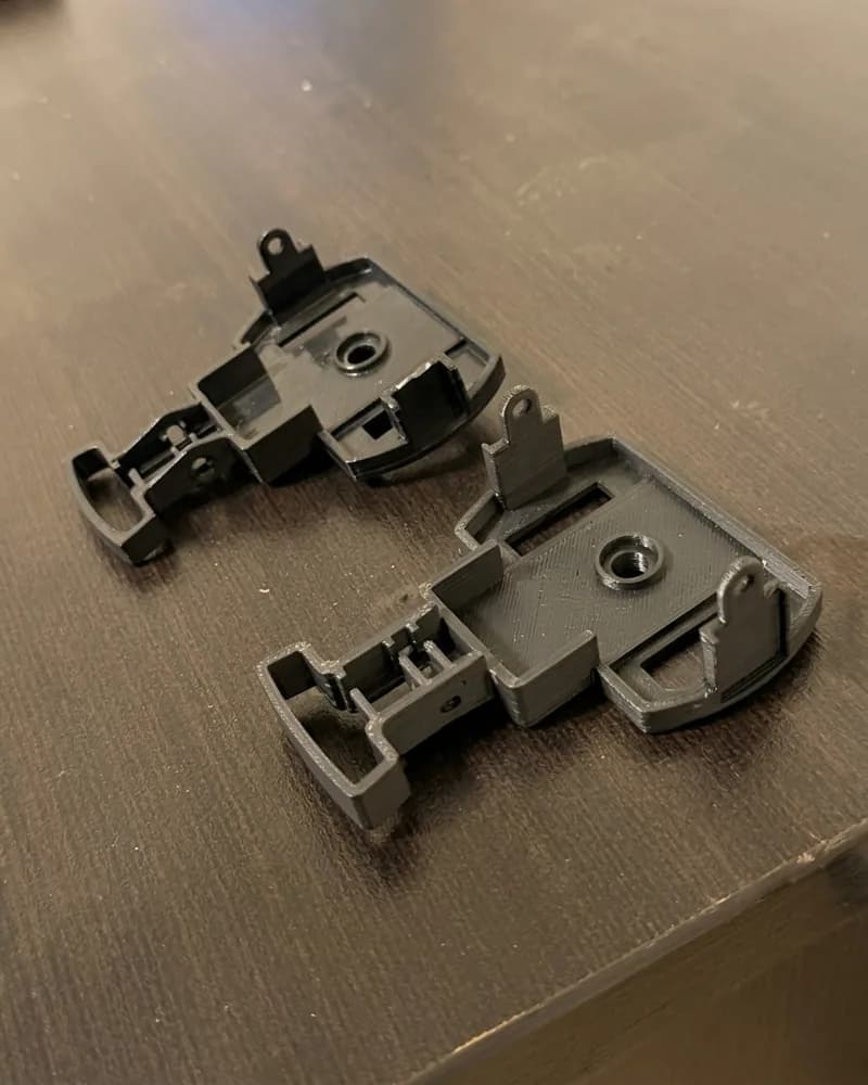 Two dark grey 3D-printed replacement brackets on a wooden table