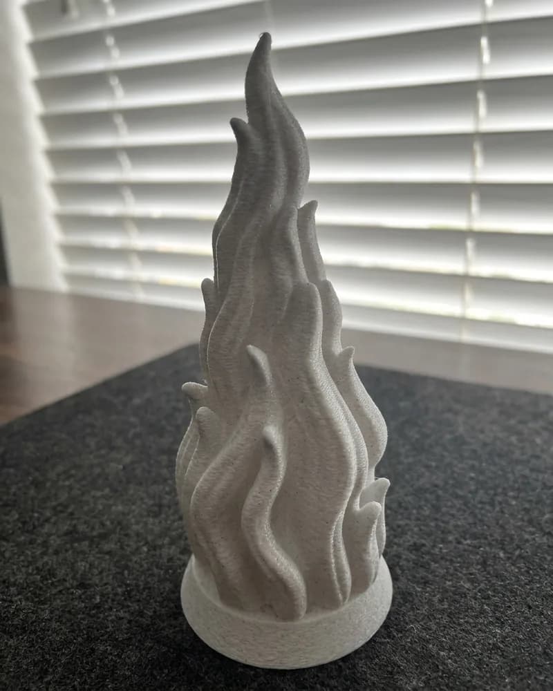 A tall white 3D-printed flame sculpture on a desk