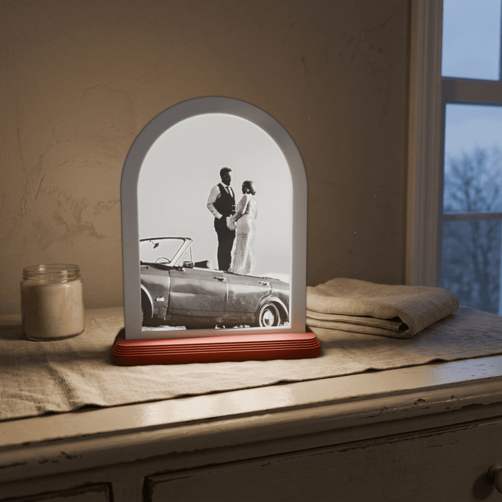 A lit arch lithophane of a couple on a vintage convertible at sunset, glowing on a nightstand